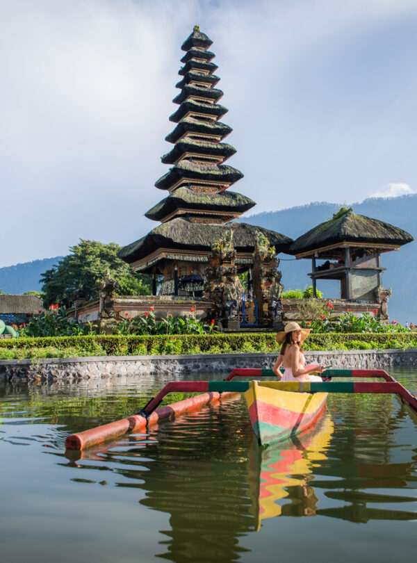 Young woman traveler paddling on a wooden boat at Pura Ulun Danu